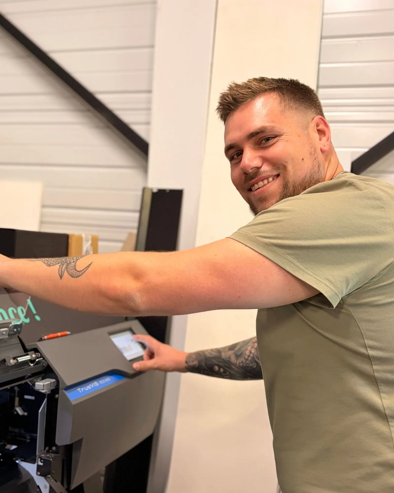 Vincent, souriant, la main sur une machine de l'atelier