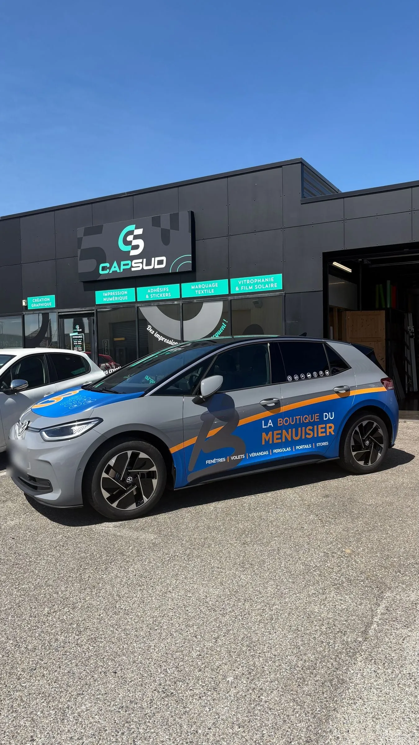 Voiture électrique grise habillée de bleu et d'orange devant l'atelier