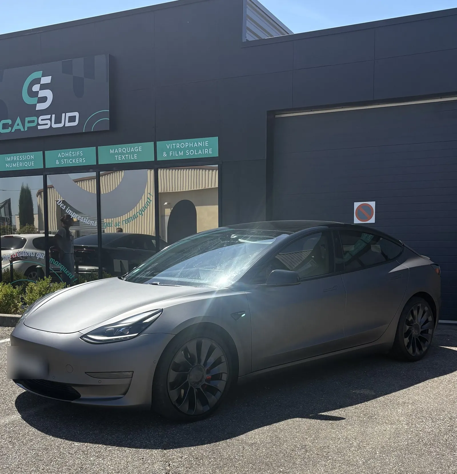 Tesla Model 3 au covering gris mat garée devant l'atelier Cap Sud